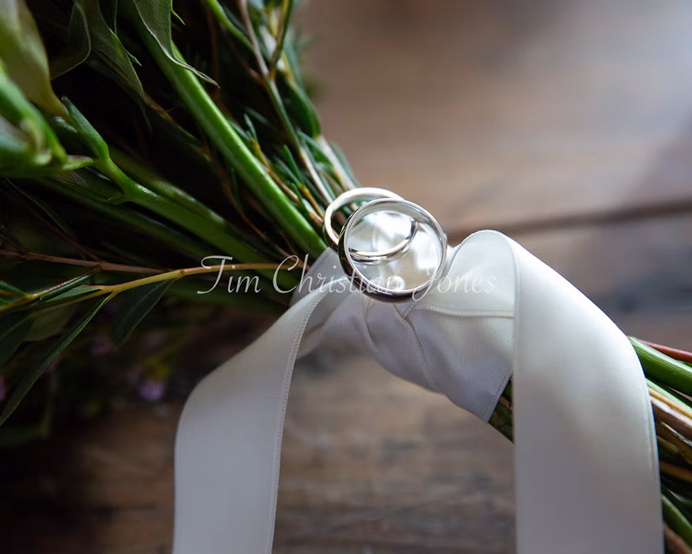 Wedding rings resting on white ribbon wrapped around the stems of a bridal bouquet.