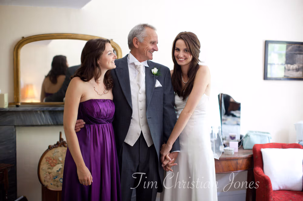 Bride standing with her father and sister, a relaxed family moment full of genuine connection.
