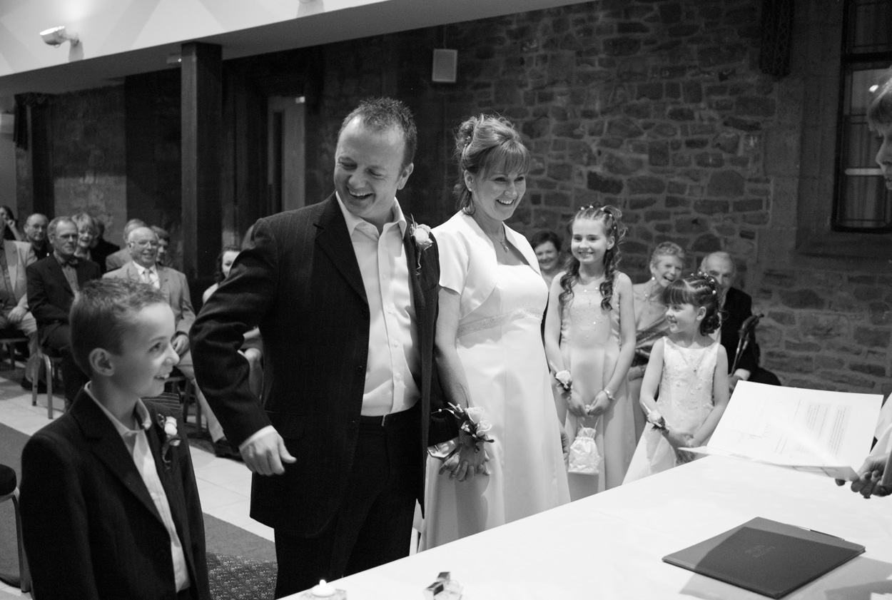 Karen & Guy smile as their young son, the pageboy, shares a joyful moment during their family wedding ceremony at Stirk House Hotel in Lancashire.