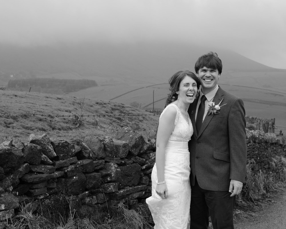Susie and Dan sharing a joyful portrait on Pendle Hill beneath dramatic grey skies as light rain falls after their Barley Village Hall wedding.