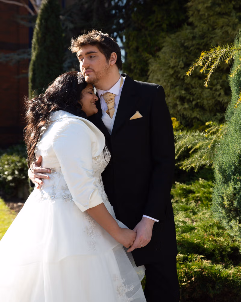 Zehra and Richard sharing a couple portrait beside the green and trees at the Crowne Plaza Leeds