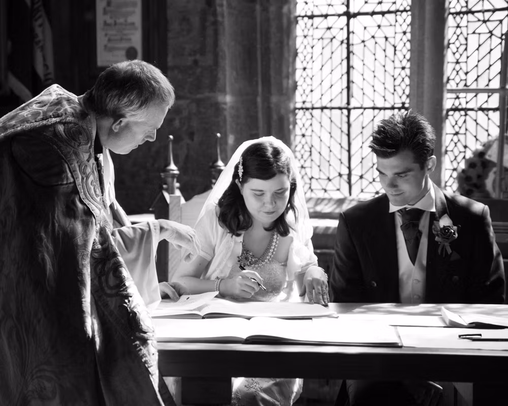 Claire and Tom signing the wedding register in the vestry at Halifax Minster - monochrome emotive moment surrounded by gothic stone.