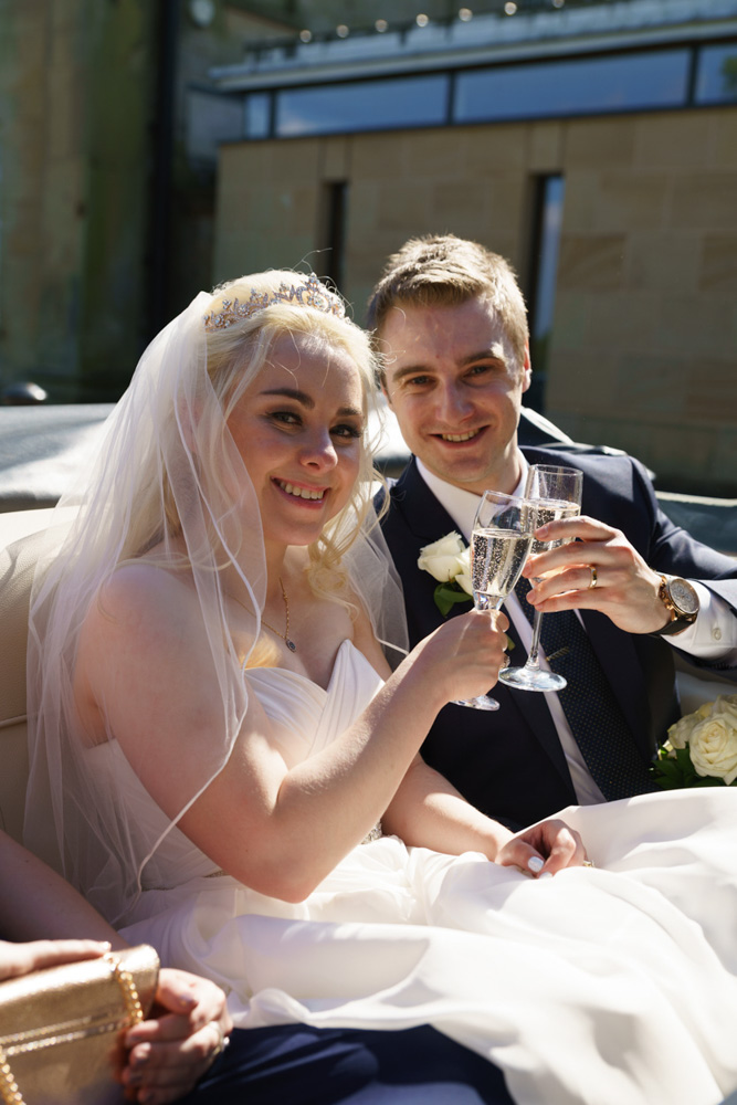 Holly and James sit with champagne and smiles in their vintage wedding car outside The Met Hotel, Leeds, after their Leeds Cathedral wedding.