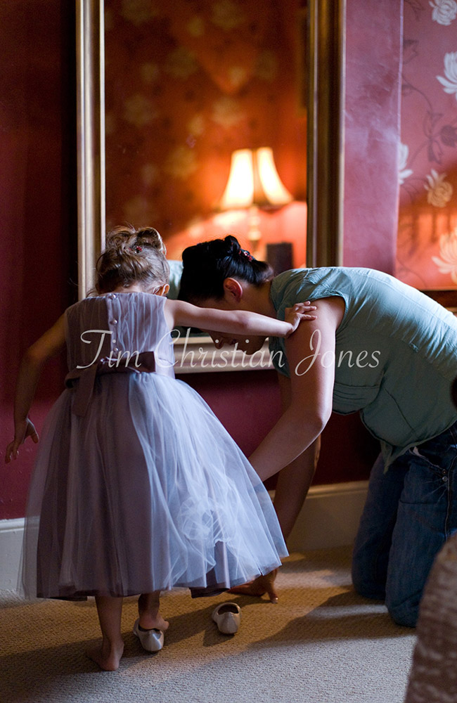 Aunty helping her little neice put on her bridesmaid shoes by the mirror in the bridal suite.