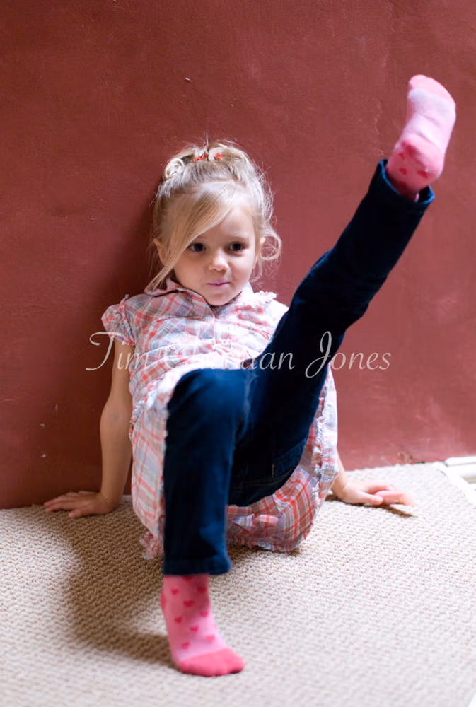 Young bridesmaid strikes a playful pose against the red wall in her party dress.