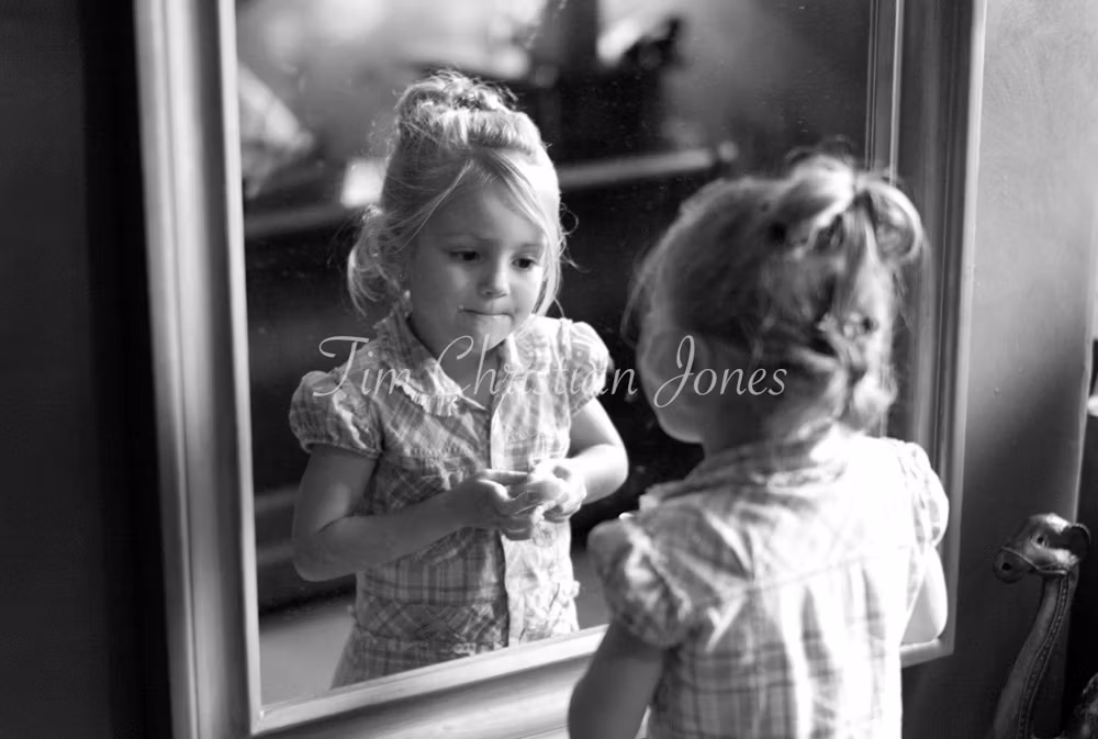Young girl checks her makeup with focus and flair in black and white.
