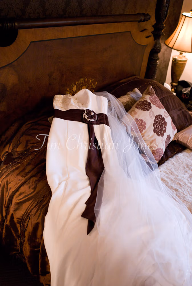 Bridal gown laid out on the bed at Woodborough Hall, detailed with lace and a deep red ribbon.