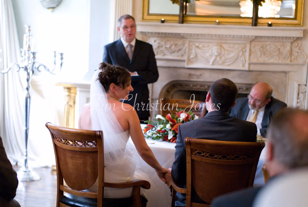 During the ceremony, the bride gently reaches to touch the groom’s hand as the registrar speaks.