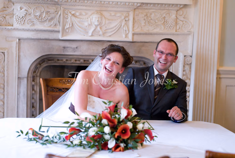 Julie and Pat laugh while pretending to sign the register, joy radiating between them.