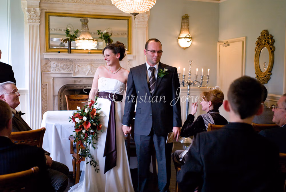 Julie and Pat leave the ceremony with relaxed smiles, bouquet swinging at her side.