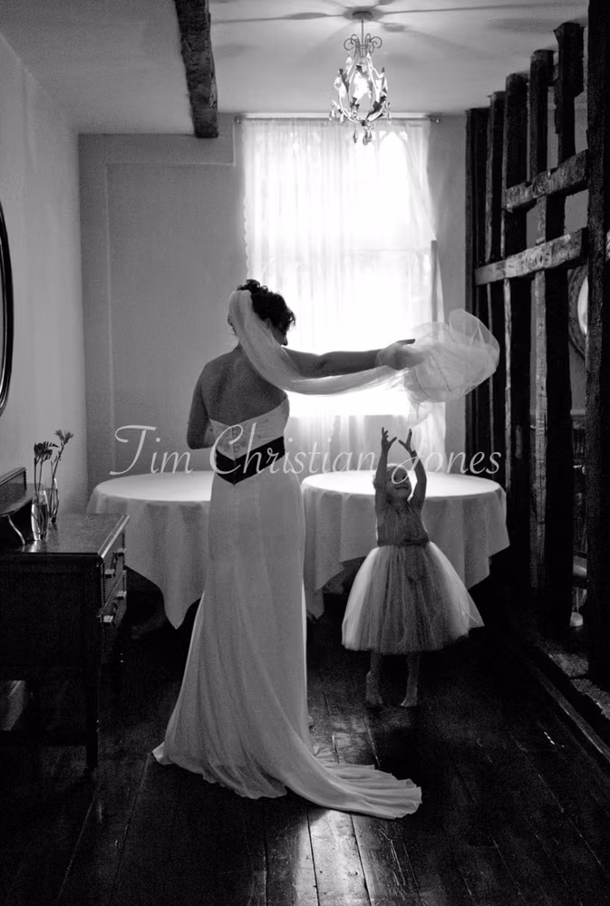 Julie lifts her veil playfully as her young daughter jumps up, reaching with delight.