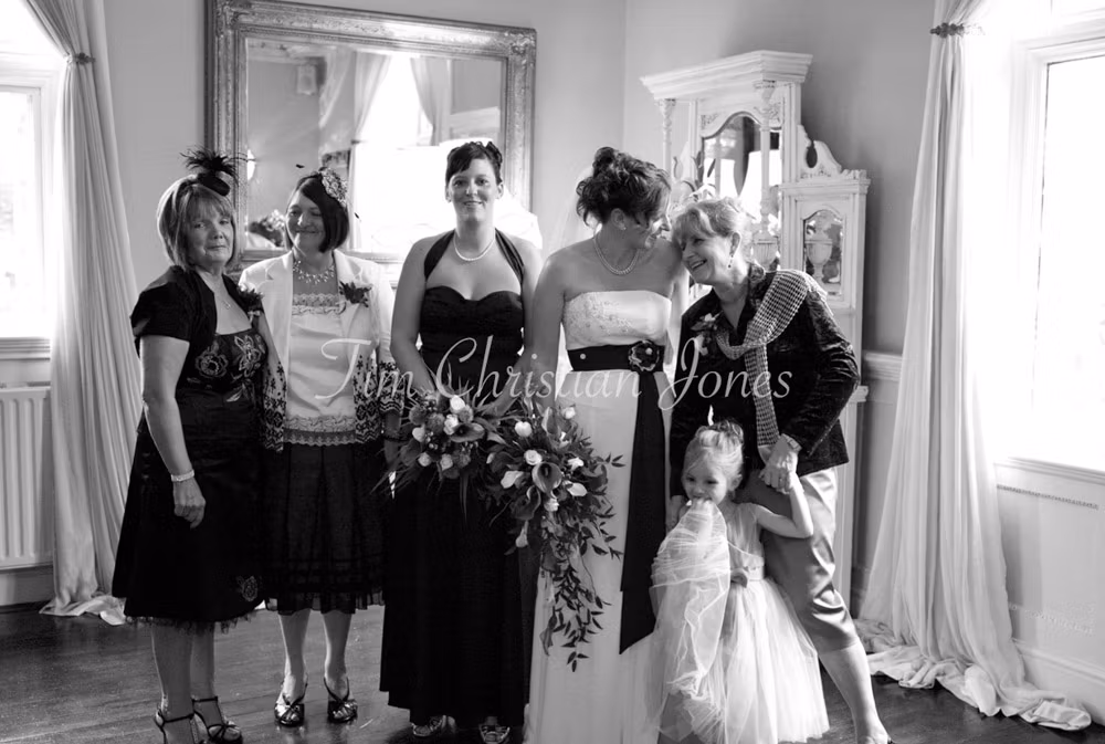 A black and white group portrait indoors at Woodborough Hall, framed by soft curtains and vintage décor.