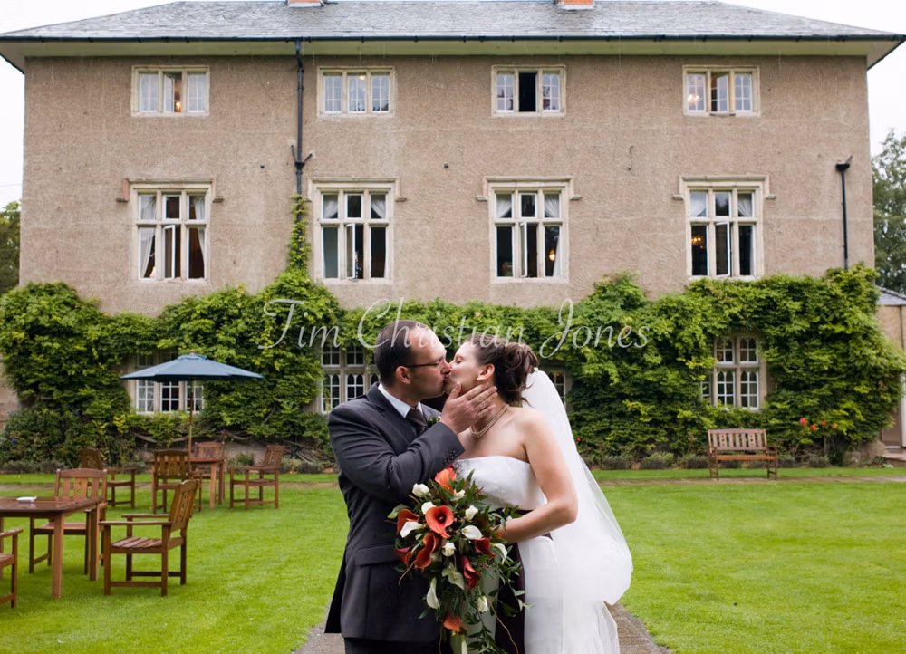 The couple share a kiss on lush, rain-fed grass with Woodborough Hall in the background.