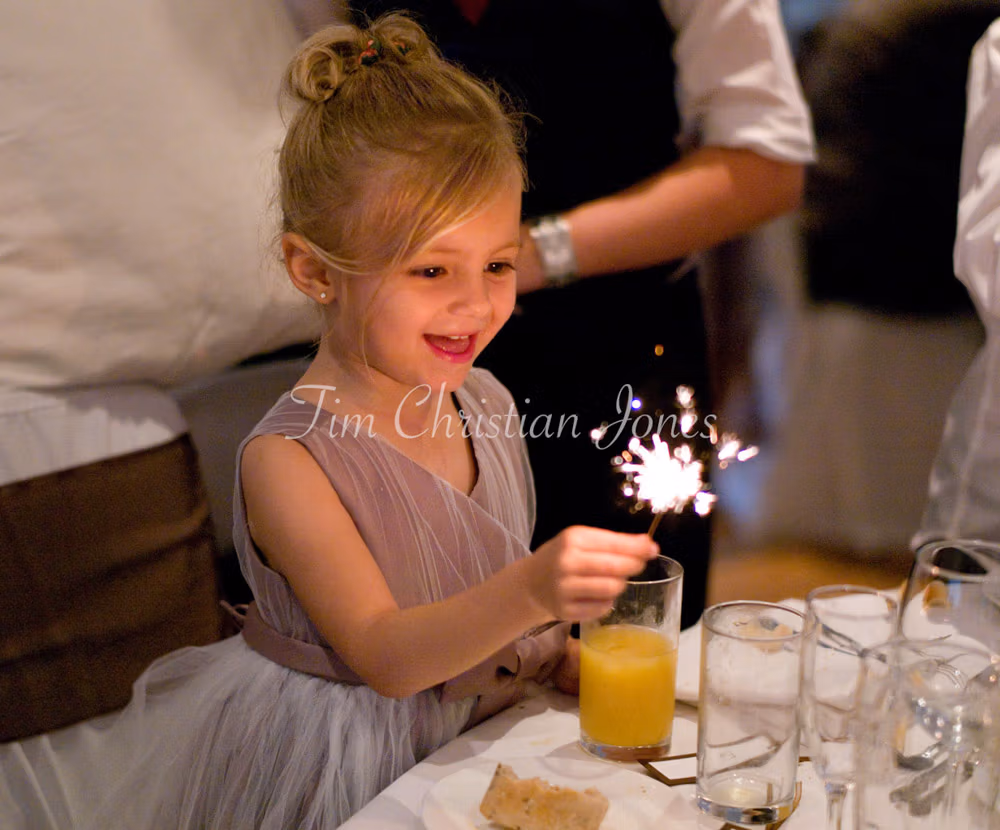 Julie and Pat’s daughter holds a sparkler at their Woodborough Hall wedding breakfast, her face glowing with delight.