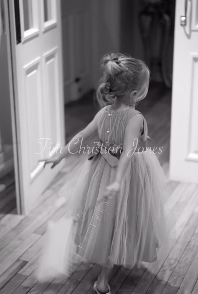 The little bridesmaid rushes joyfully through a doorway, dress swirling behind her.