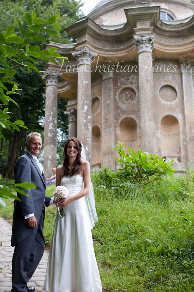 Bride walks with her father along the stone path to the Temple of Apollo, looking back for a photo