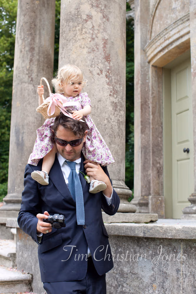 Flower girl sits on her dad’s shoulders in the gardens
