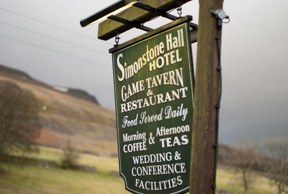 The historic Simonstone Hall Hotel sign stands beneath dramatic February skies overlooking the rolling hills of Wensleydale before Alison and Hamish's Yorkshire Dales wedding begins.