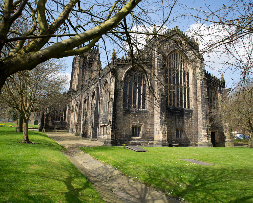 Halifax Minster’s grand facade lit by spring sunshine, framed by trees and daffodils.