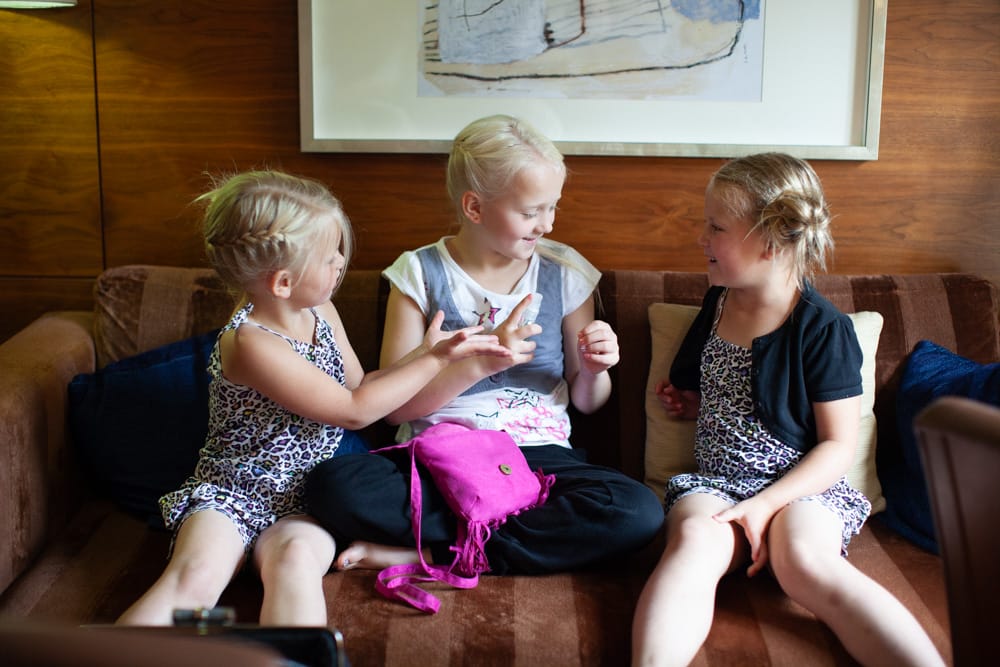 Three young girls sit together on the sofa, sharing hand sanitiser and giggles before the wedding.