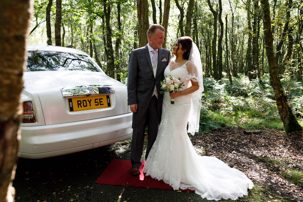 Bride and father beside a white Rolls-Royce outside the lodge at Chevin Country Park Hotel, train spread and bouquet in hand.