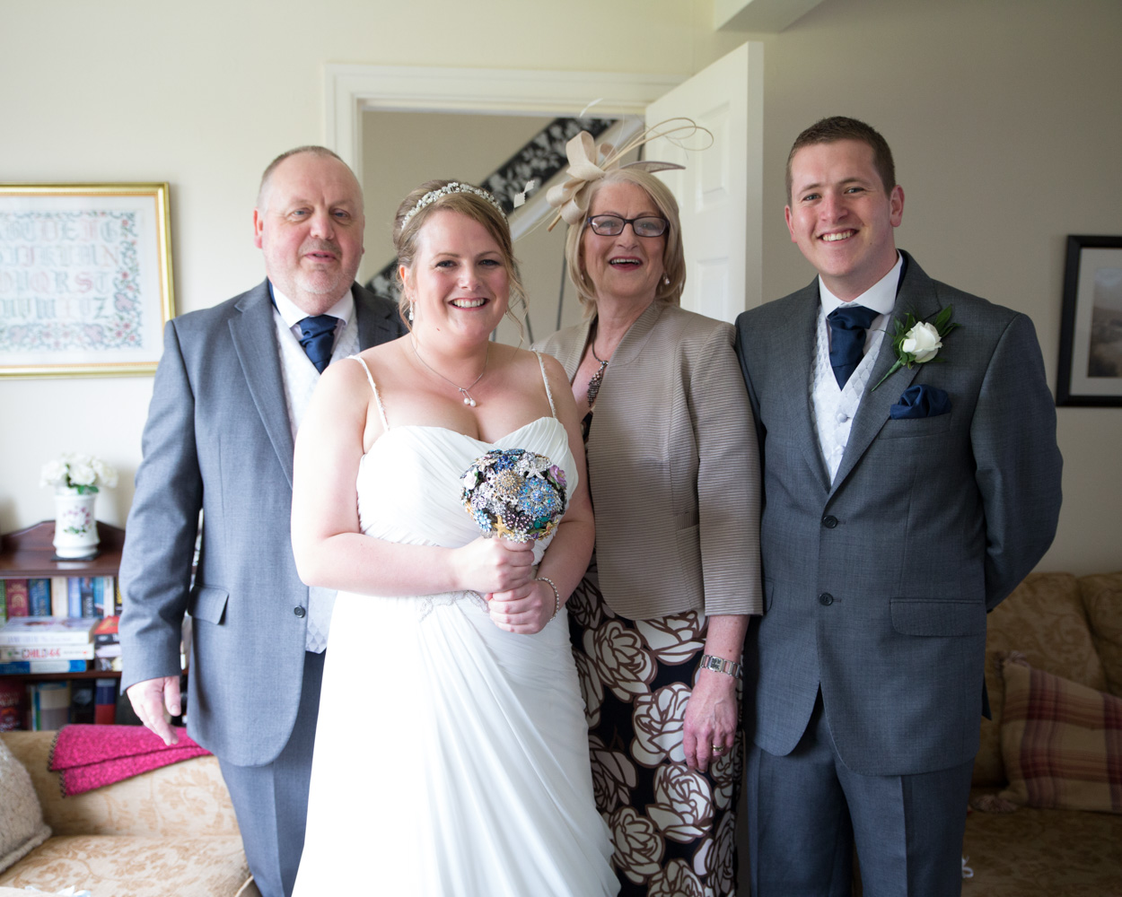 Relaxed family group photo at home before a Scarborough wedding, with the bride smiling alongside her parents and brother.