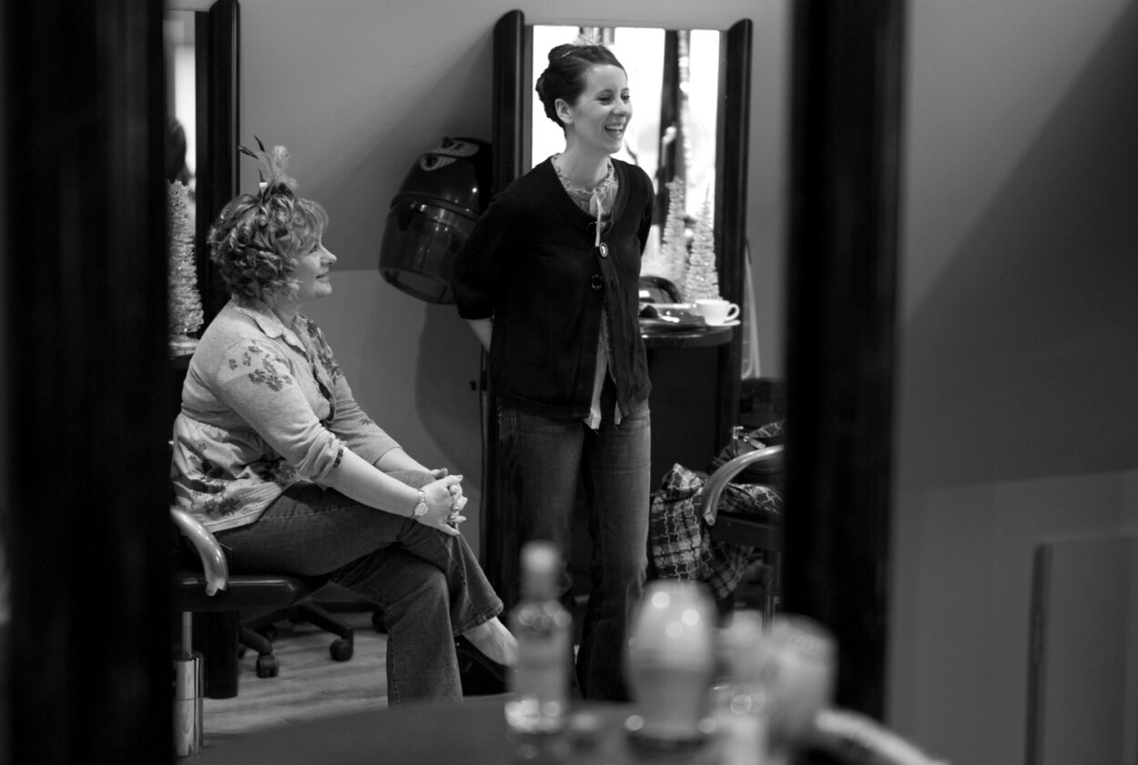 Reflection of Emelie smiling in the mirror as her mum looks up with pride.