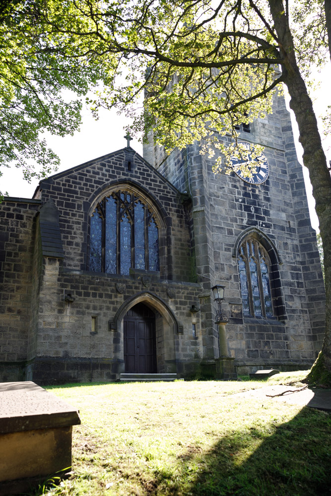 St Oswald’s Church Guiseley in summer light, framed by trees and dappled shadows.