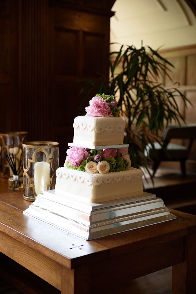 Three-tier wedding cake with a floral middle tier, placed on an oak table in the great hall.