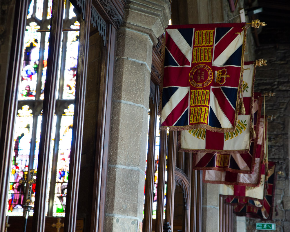Six flags hang in a row inside Halifax Minster, catching the ambient light.