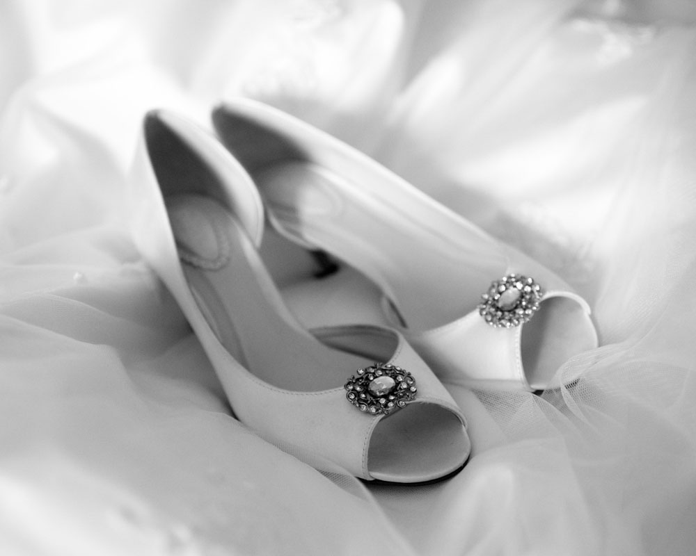 Black and white photo of wedding shoes placed on the wedding dress.