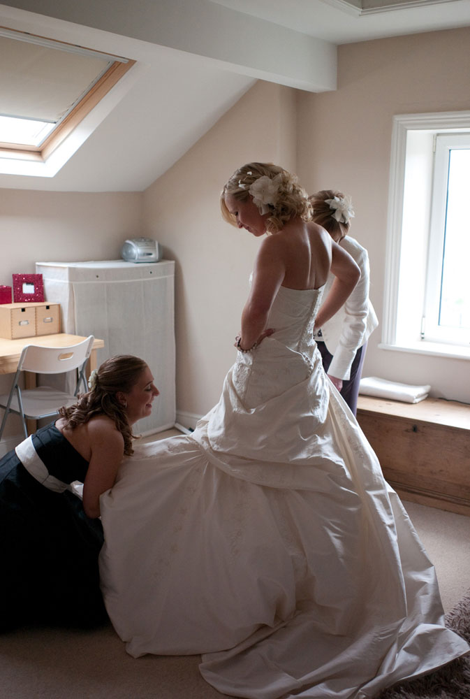 Bridesmaid kneels to help Dani with her shoes in the attic dressing room