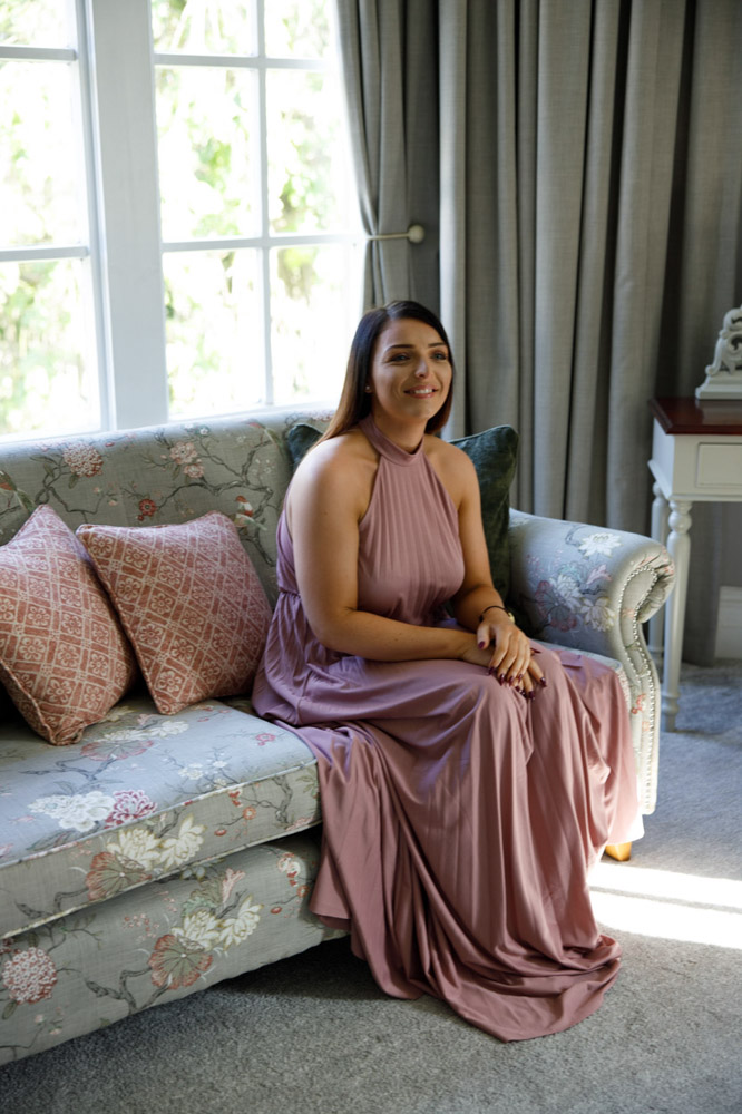Bridesmaid seated on a sofa in a stylish pink dress, relaxing before the ceremony