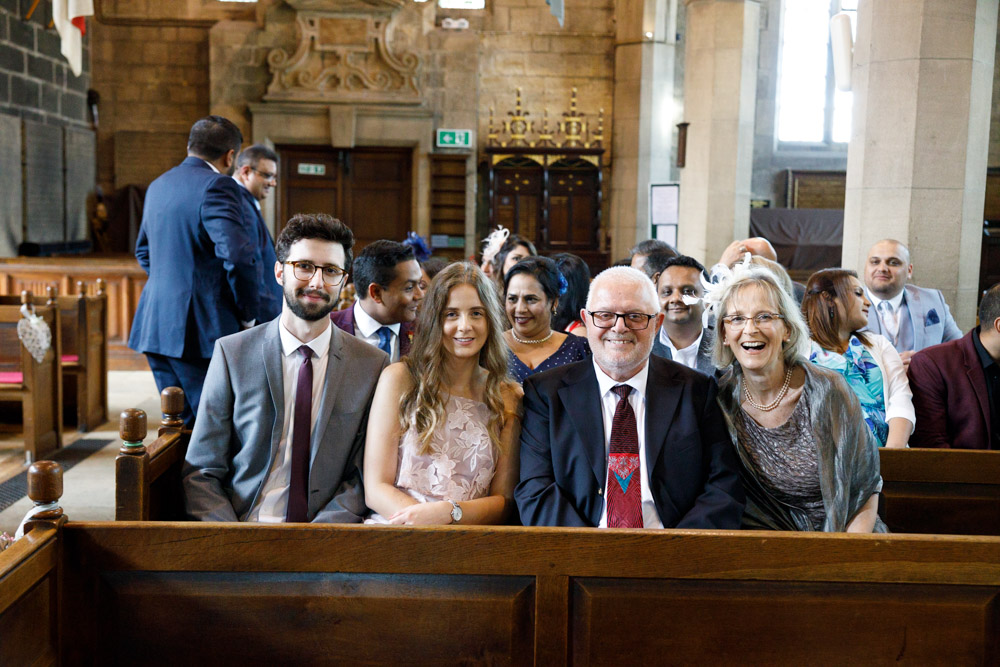 Wedding guests seated inside St Oswald’s Church, smiling toward the aisle.