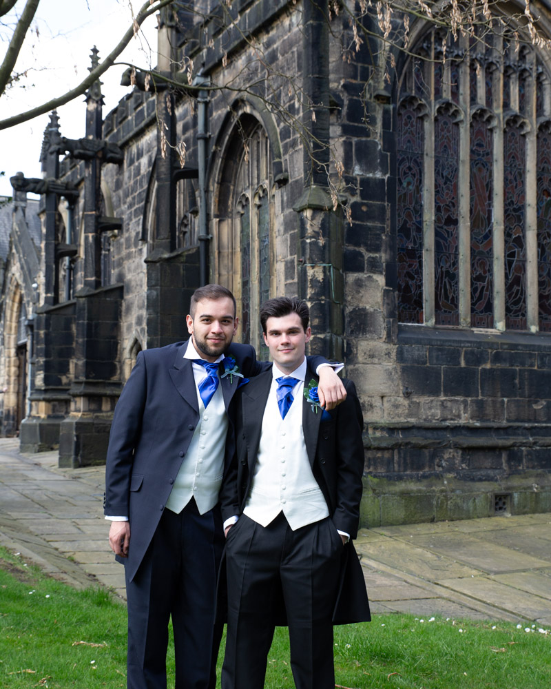 The groom and best man in blue ties and tuxes, standing in the sunlight before the ceremony.