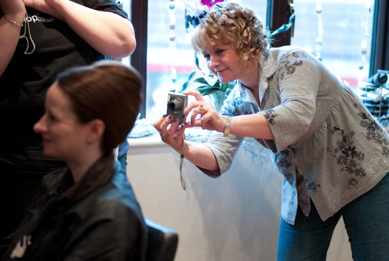 Mother of the bride photographs her other daughter getting her hair styled.