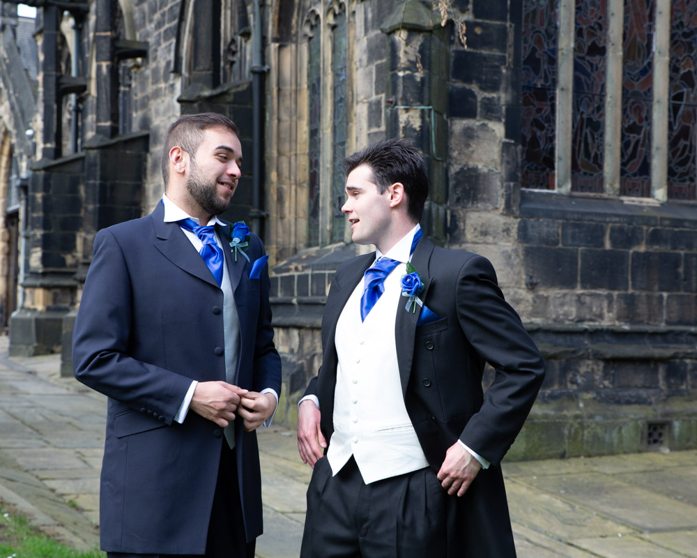 A natural shot of the groom and best man chatting and laughing outside Halifax Minster.
