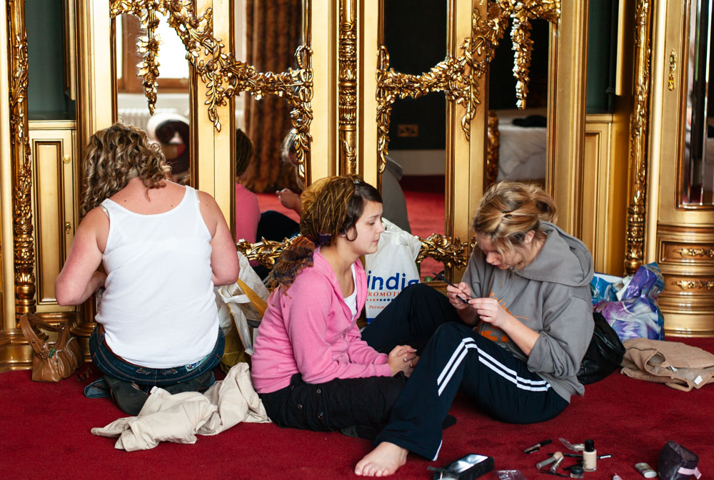 Bridesmaids doing makeup on the carpet beside gold-accent wardrobes