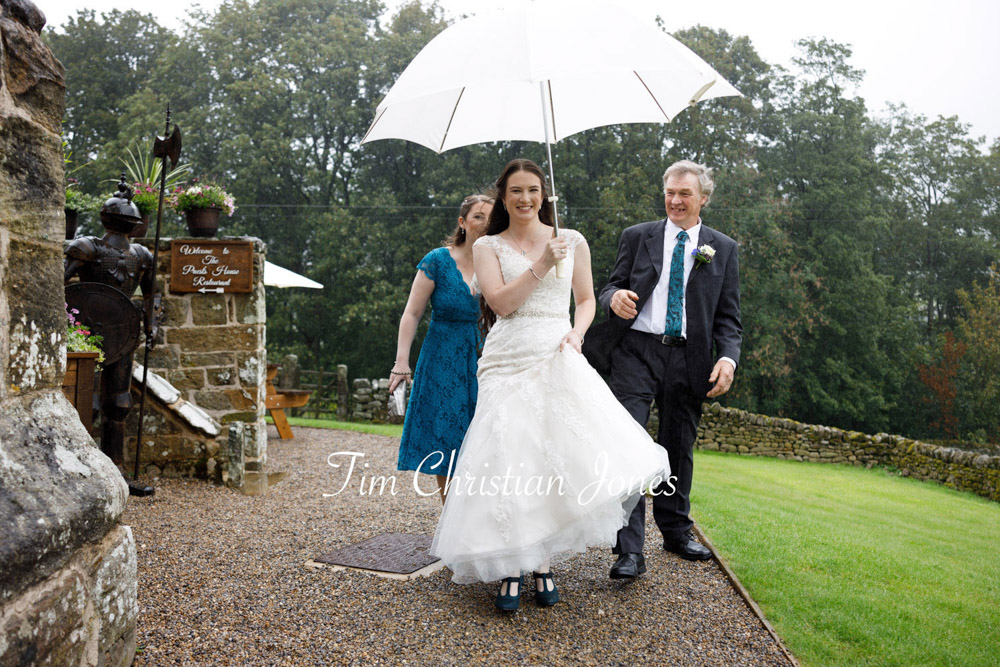 Natural candid wedding moment in Yorkshire: bride and family with umbrella
