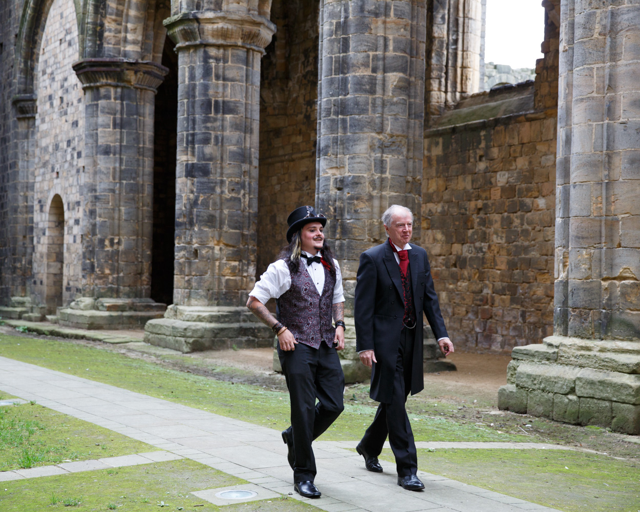 The groom’s father and brother walk together down the long aisle toward the ceremony space