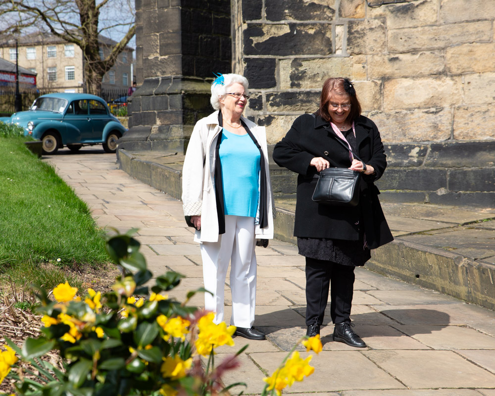 Two more guests stroll toward the minster in bright sunshine, laughing together.