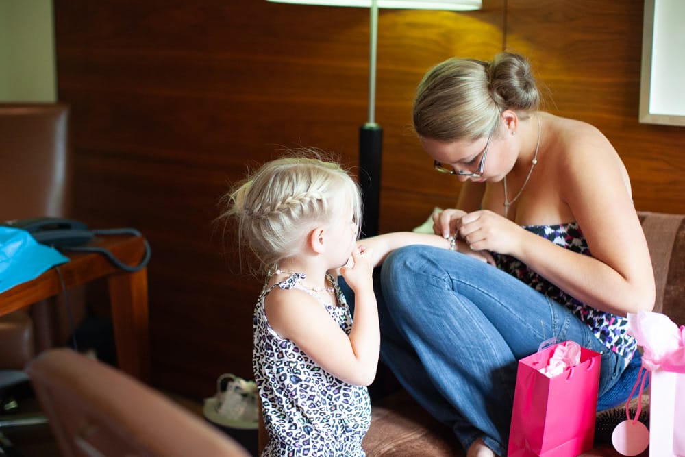 Teenage bridesmaid helps her younger sister fasten a bracelet.