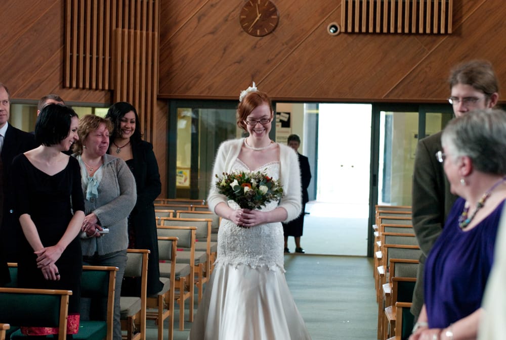 Bride smiling brightly walking down the aisle at St George’s Church in Leeds.