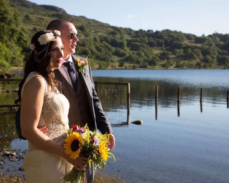 Wedding couple by a calm lake at golden hour, sharing a quiet moment together