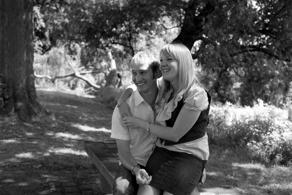 Carly and Lee smiling on a weathered bench in soft black and white light at Kirkstall Abbey.