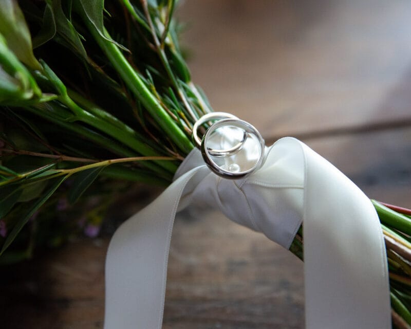 Wedding rings tied to a bouquet ribbon in soft light