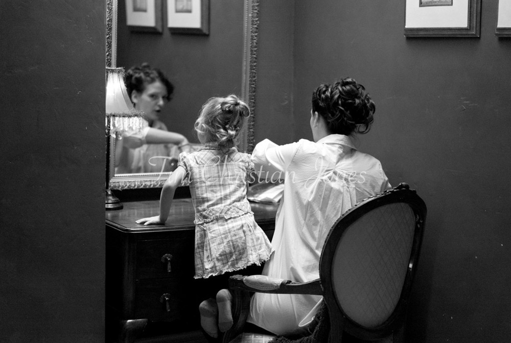 Mother and daughter share a quiet makeup moment by the mirror in soft black and white.