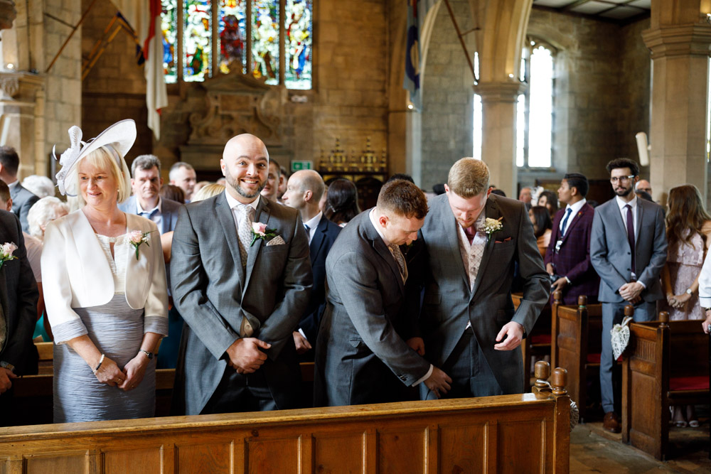 Groom and best men stood at the front of the church, sharing a smile before the ceremony starts.