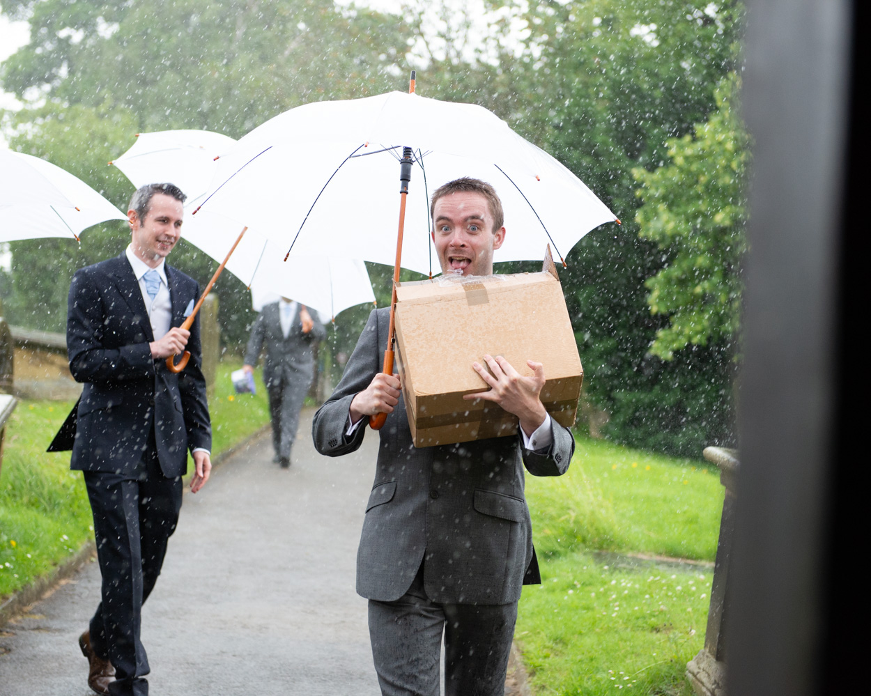Groom and groomsmen arrive holding white umbrellas in the rain