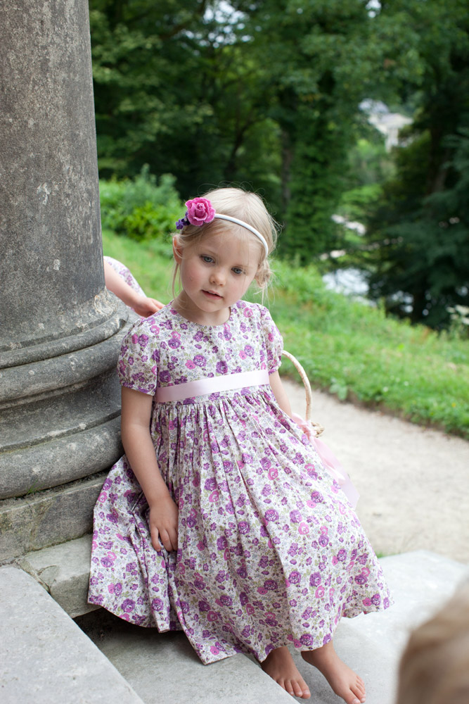 Little flower girl resting on the stone steps, surrounded by summer greenery